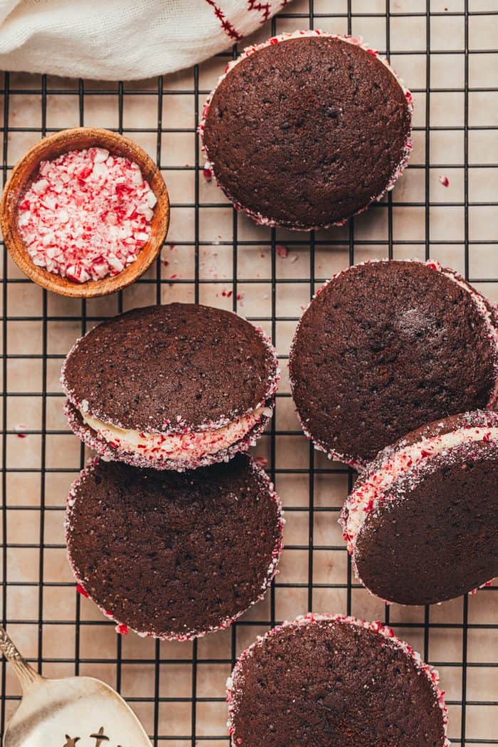 A variety of chocolate Whoopie pies on a cooling rack coated with crushed peppermint candies.
