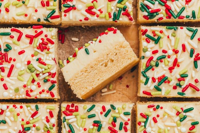 Frosted sugar cookie bars sliced showing the top of the bar with sprinkles. One bar is flipped on its side showing the bar and the thick frosting.