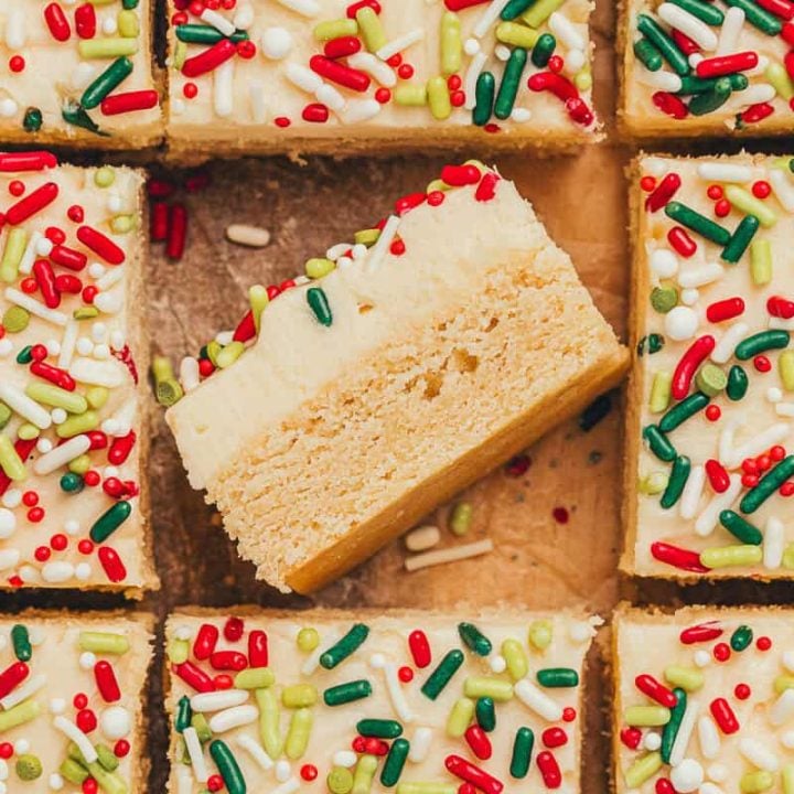 Frosted sugar cookie bars sliced showing the top of the bar with sprinkles. One bar is flipped on its side showing the bar and the thick frosting.