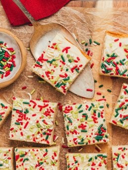 Frosted sugar cookie bars sliced showing the top of the bar with sprinkles. One of the bars is on a spatula.