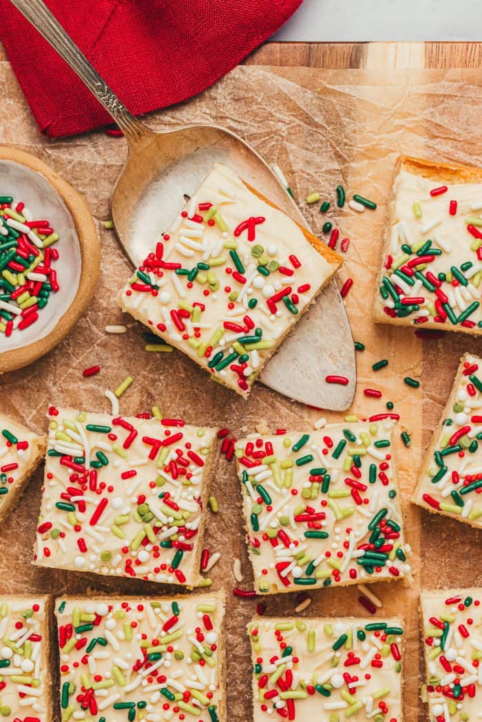 Frosted sugar cookie bars sliced showing the top of the bar with sprinkles. One of the bars is on a spatula.