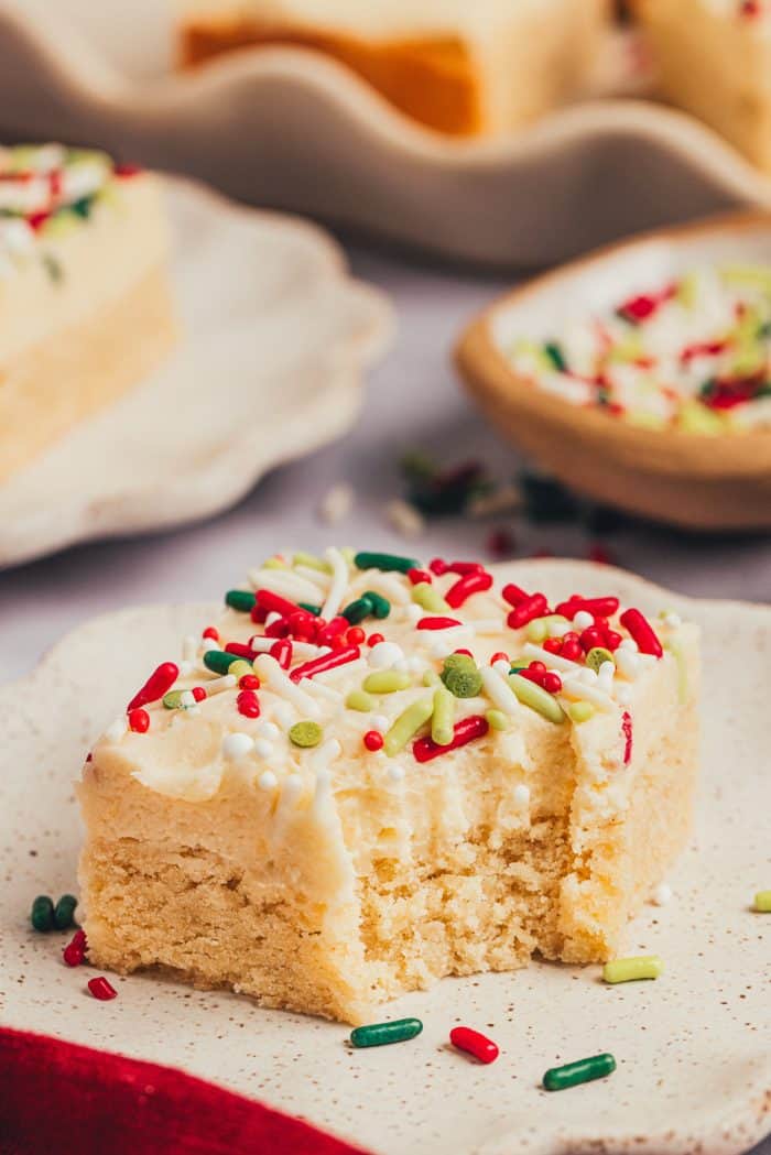 A sugar cookie bar with a bite taken out of it on a plate.