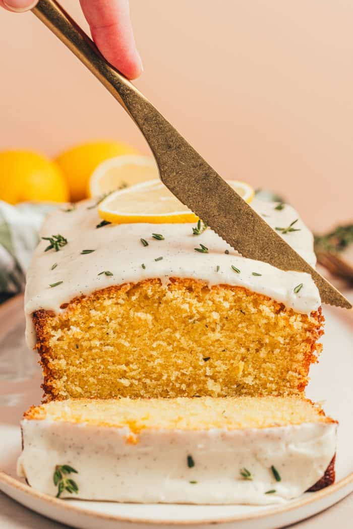 A platter with a loaf of lemon pound cake with slices of the cake and fresh thyme sprinkled around it.