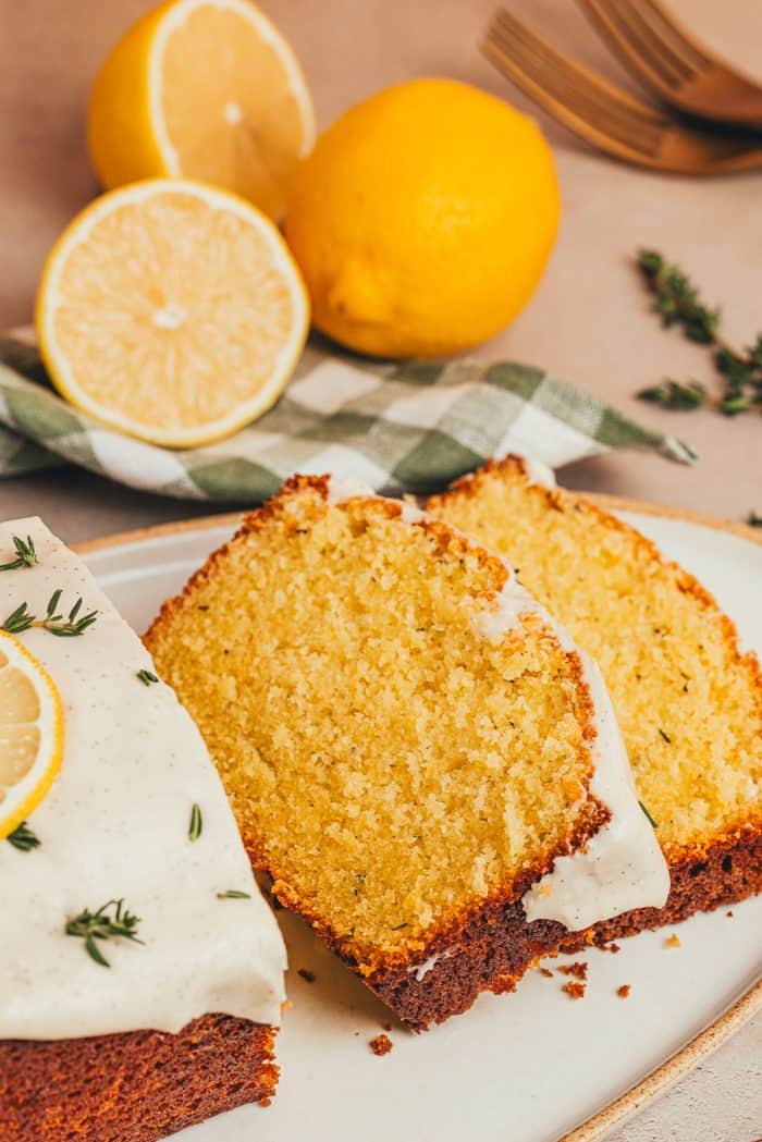 A platter with a loaf of lemon pound cake with slices of the cake and fresh thyme sprinkled around it.