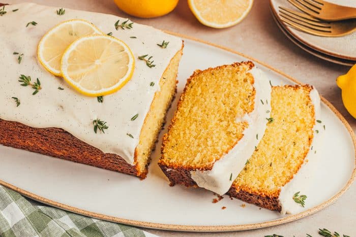 A lemon Thyme cake loaf cut into slices on a platter.