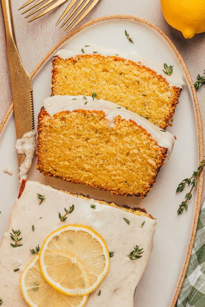 A platter with a loaf of lemon pound cake with slices of the cake and fresh thyme sprinkled around it.