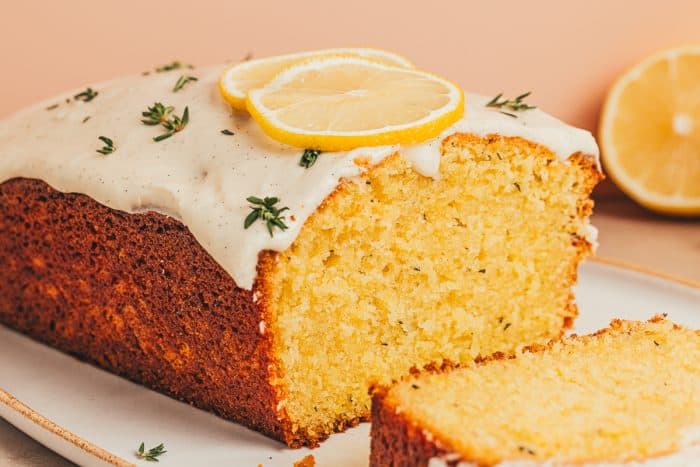 A lemon Thyme cake loaf cut into slices on a platter.