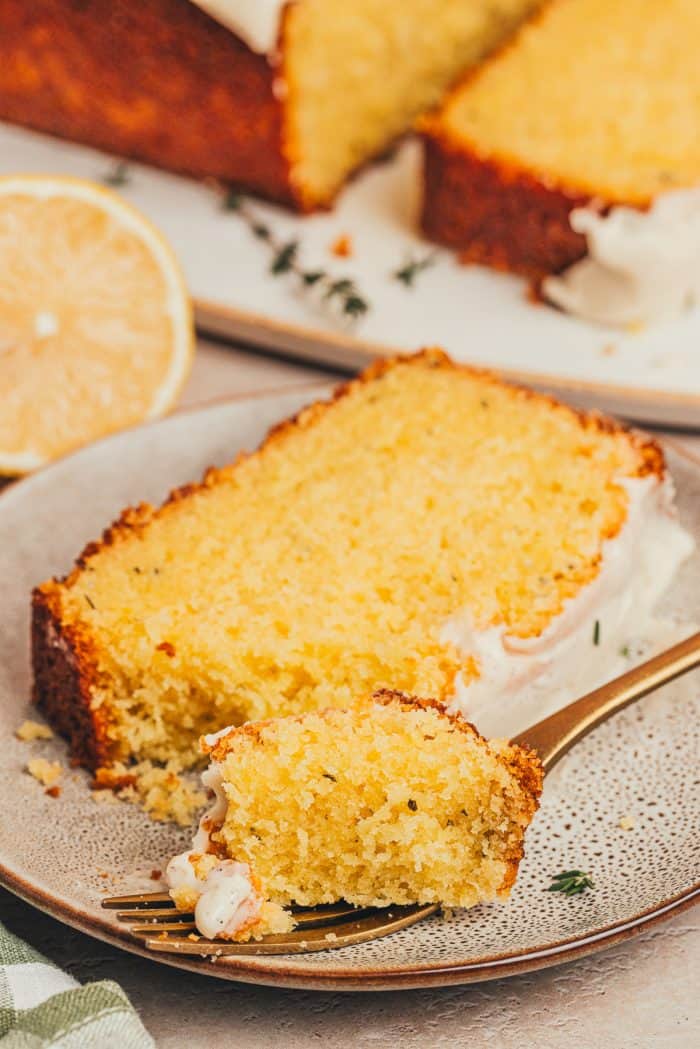 A slice of lemon thyme loaf on a plate with a fork taking a bite out of it.