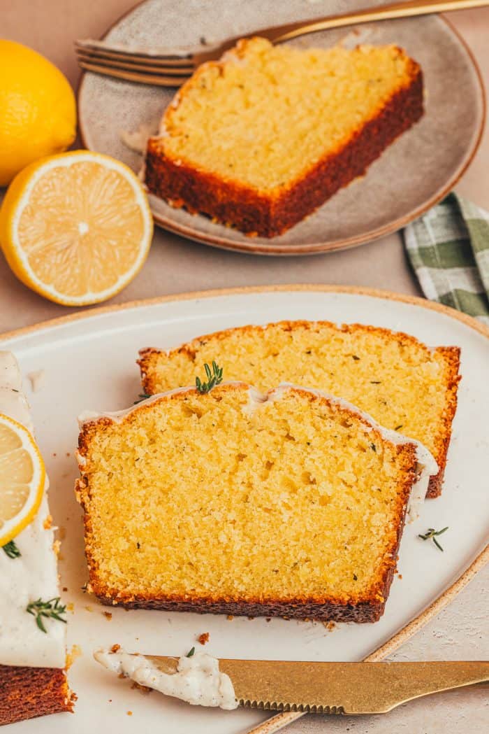 Two slices of lemon pound cake on a plate with lemons cut in half in the background.