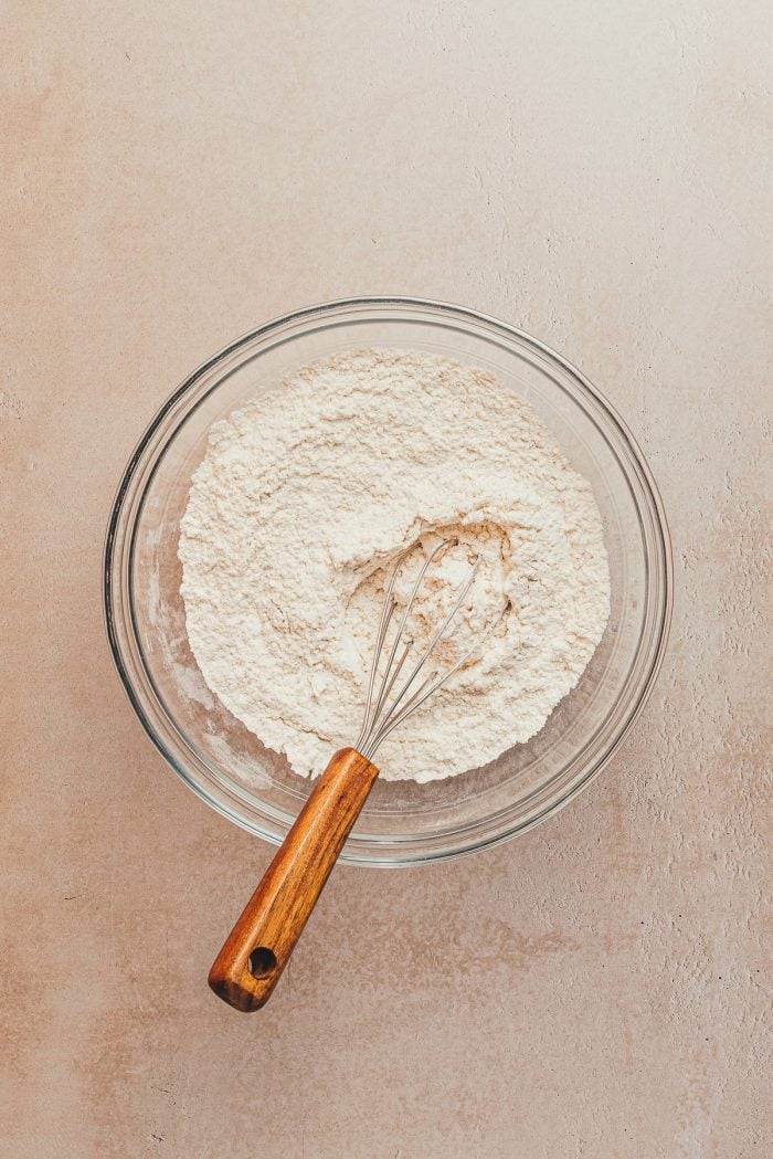 A glass bowl with the dry ingredients and a whisk.