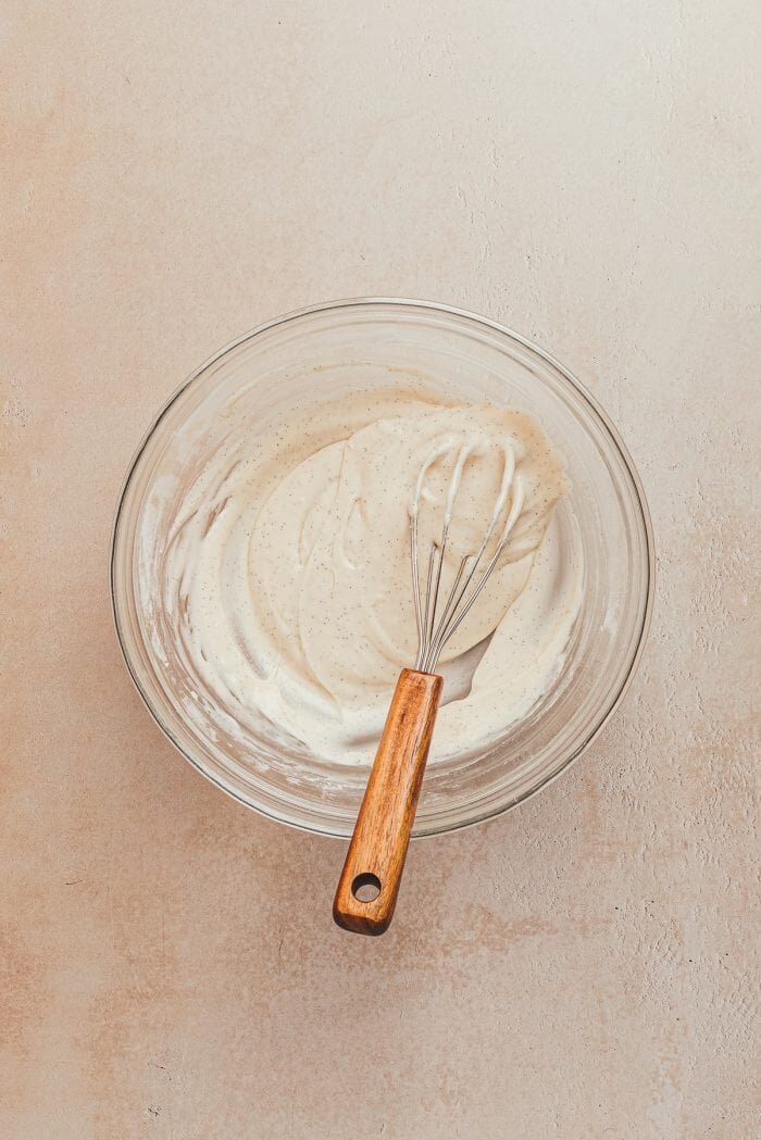 A glass bowl with the lemon icing and a whisk.