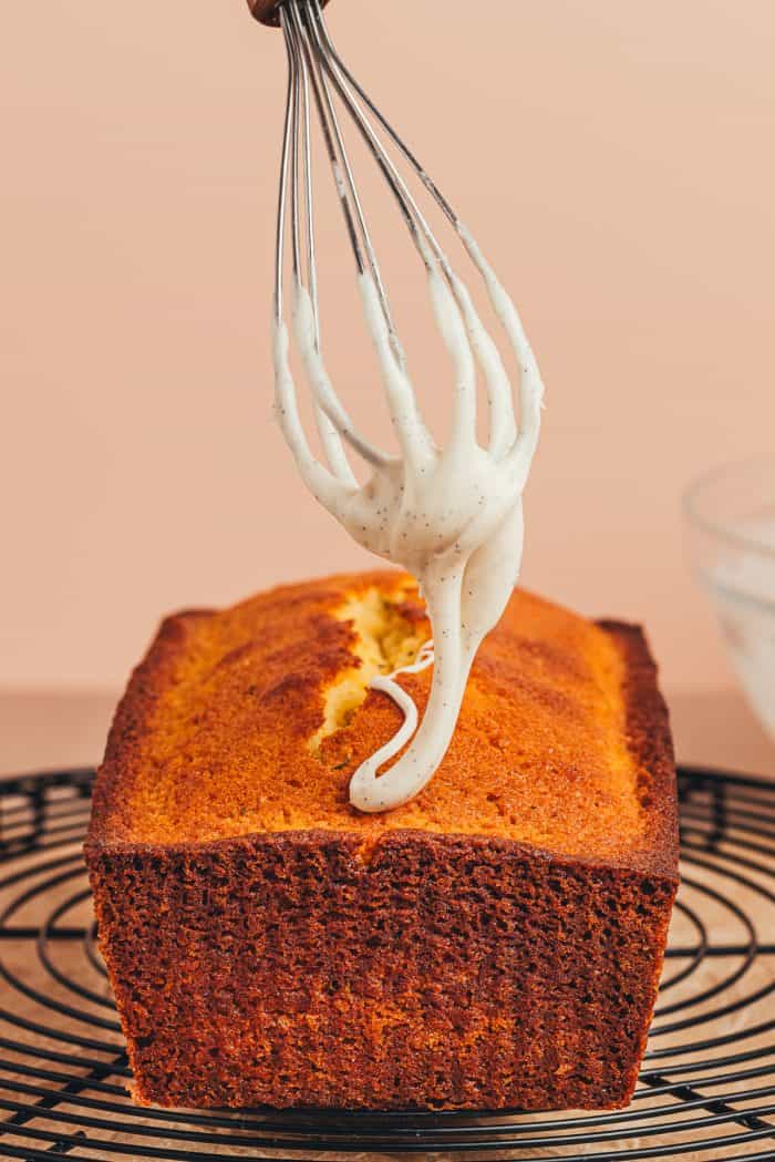 Icing being drizzled with a whisk over a lemon thyme pound cake