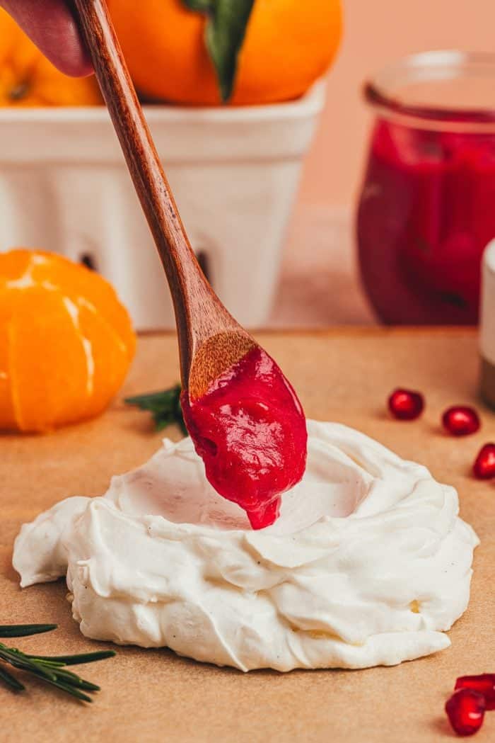 A mini pavlova with cranberry curd being spooned into it.