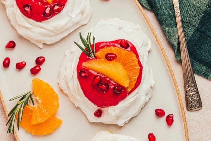 Two mini pavlovas with cranberry curd and orange slices with other garnishes on a platter.