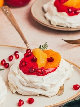 A mini pavlova with cranberry curd and orange slices with other garnishes on a platter with a cake spatula under it.