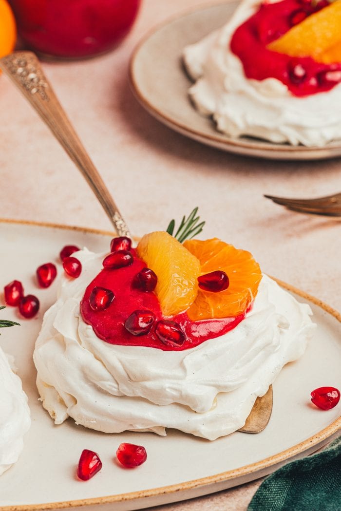 A mini pavlova with cranberry curd and orange slices with other garnishes on a platter with a cake spatula under it.