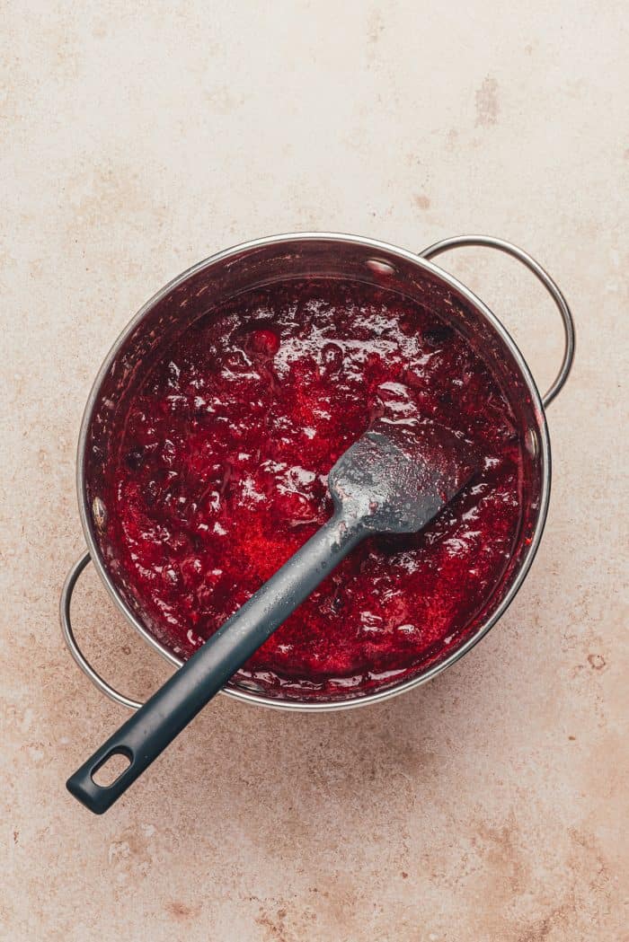 Cranberries being cooked in a saucepan with a spatula.