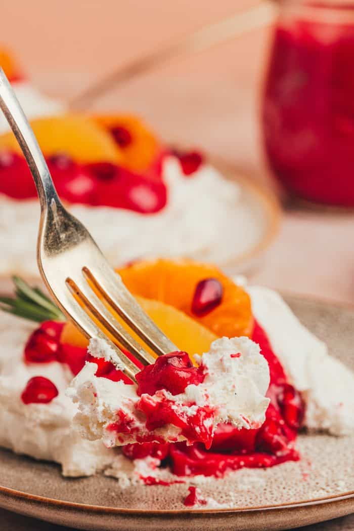 A fork taking a bite out of a mini pavlova with cranberry curd and orange slices with other garnishes.
