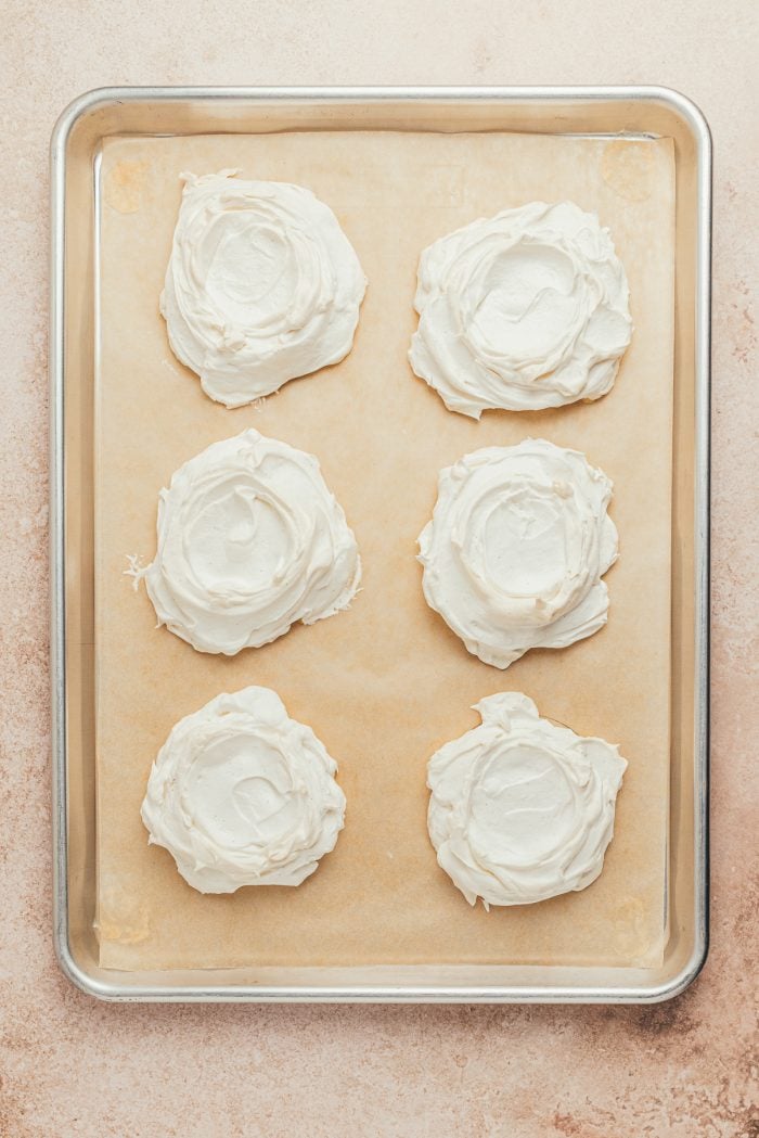 Baked mini Pavlovas on a baking sheet with parchment paper.