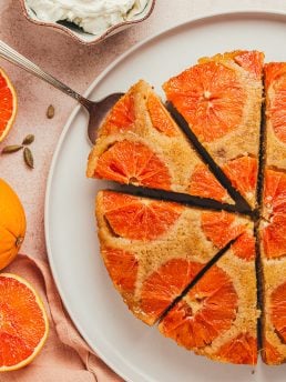 An orange upside down cake with slices cut and one slice is being lifted out of it.