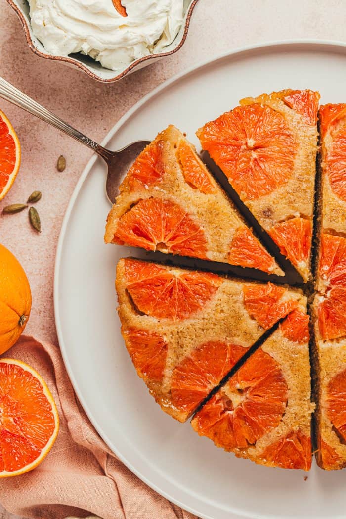 An orange upside down cake with slices cut and one slice is being lifted out of it.