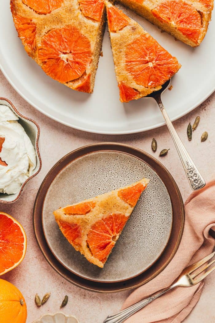 A slice of orange upside down cake on a plate and the main cake on a platter.