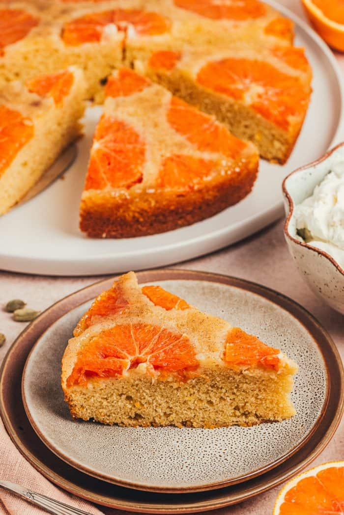 A slice of orange upside down cake on a plate and the main cake on a platter.