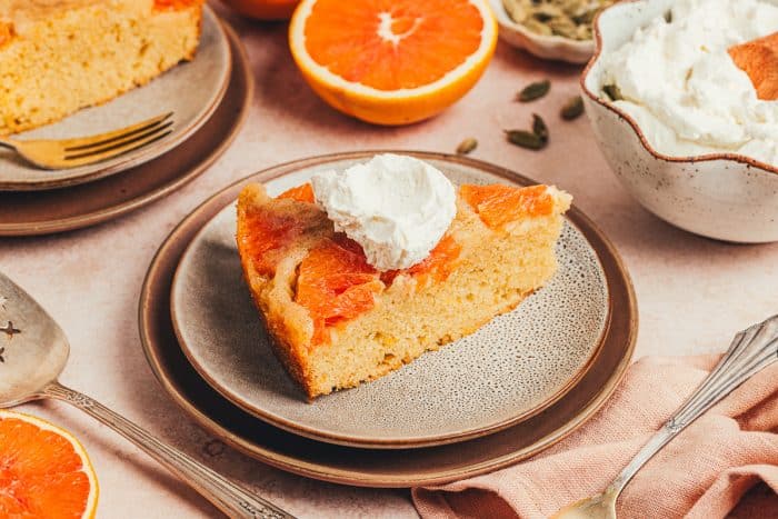 A slice of upside down orange cake on two plates with half an orange in the background.