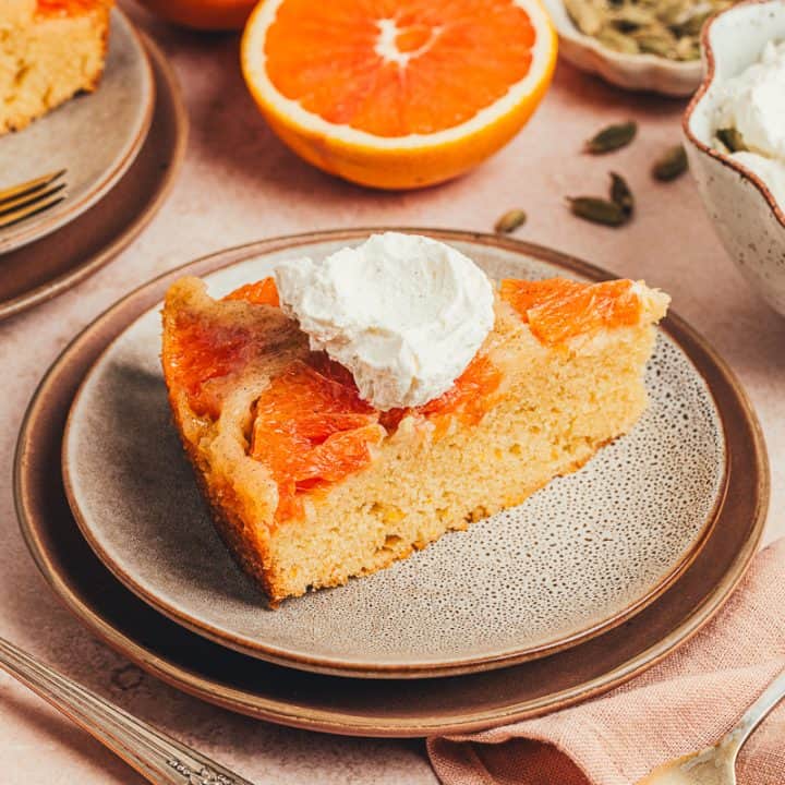 A slice of upside down orange cake on two plates with half an orange in the background.