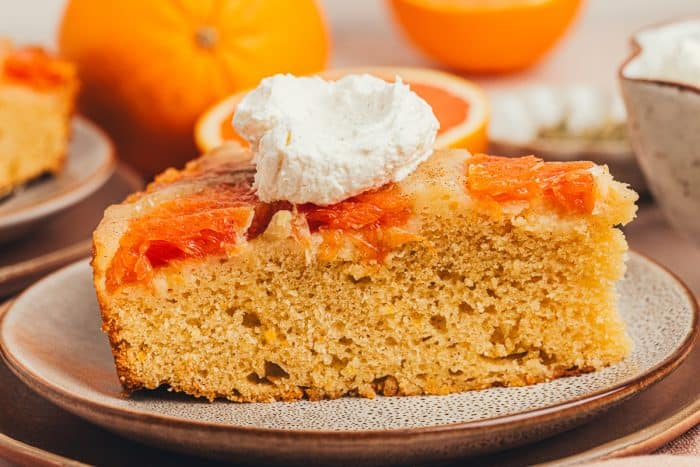 A slice of upside down orange cake on two plates with an orange in the background.