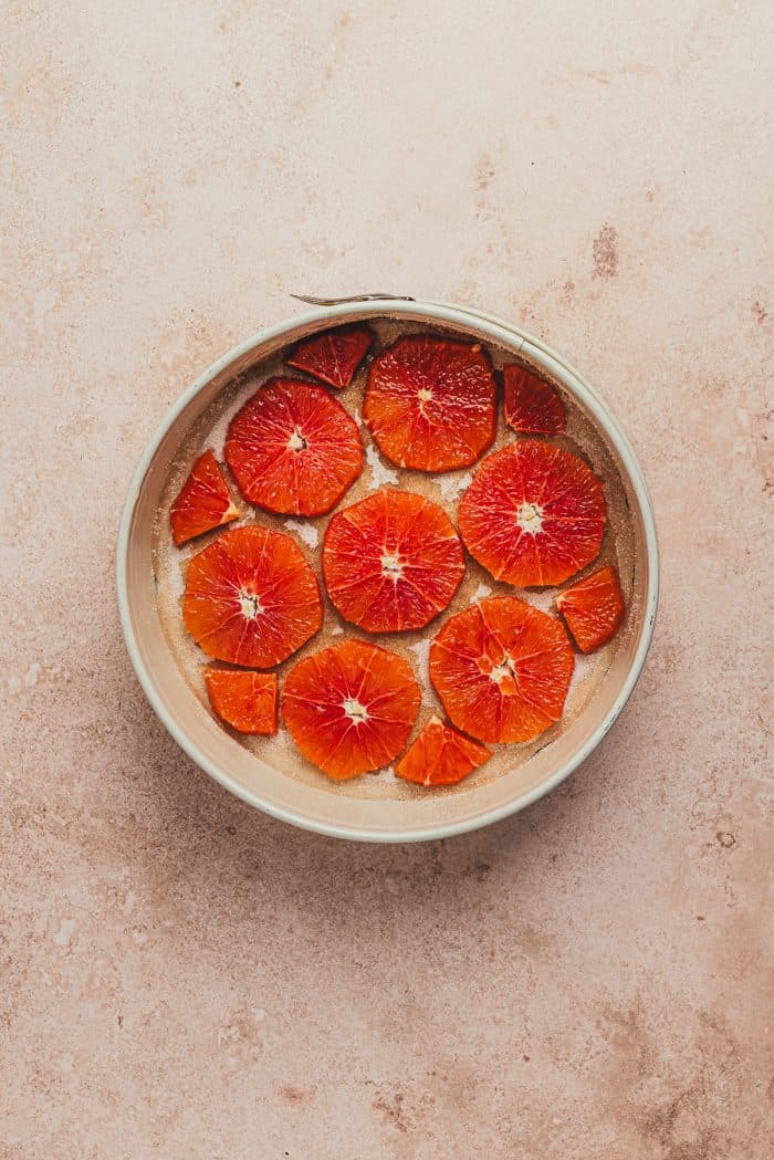 A round cake pan with sliced oranges and parchment paper.