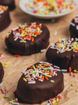 A few homemade chocolate Easter eggs scattered on parchment paper with a small plate filled with sprinkles.