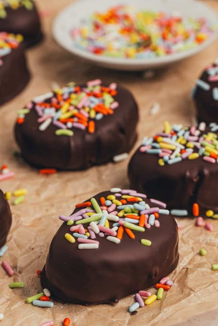 A few homemade chocolate Easter eggs scattered on parchment paper with a small plate filled with sprinkles.