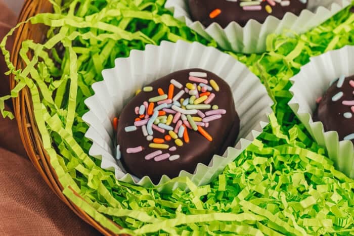 A few homemade chocolate-covered Easter eggs in confetti papers in a wicker basket with shredded green filling.