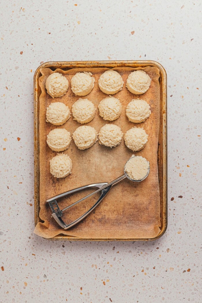 The coconut filling balls are placed on a baking sheet with parchment paper and a scoop.