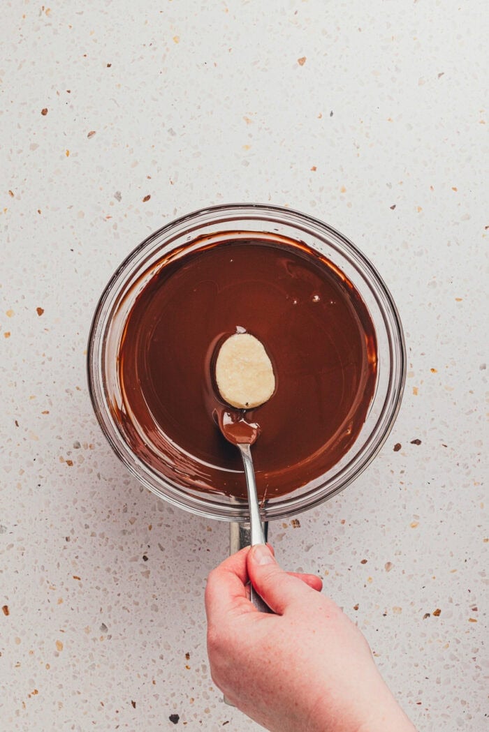 The egg-shaped filling being dipped into a bowl filled with melted chocolate.