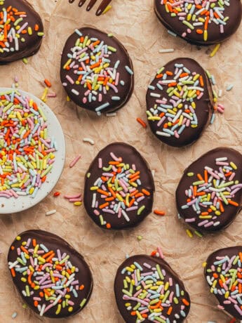 A few homemade chocolate Easter eggs scattered on parchment paper with a small plate filled with sprinkles.