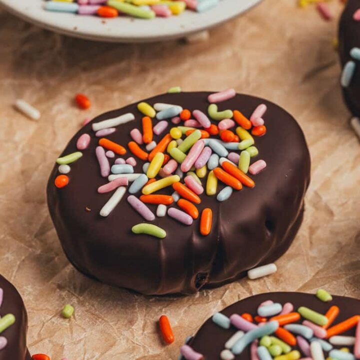 A few homemade chocolate Easter eggs scattered on parchment paper with a small plate filled with sprinkles.