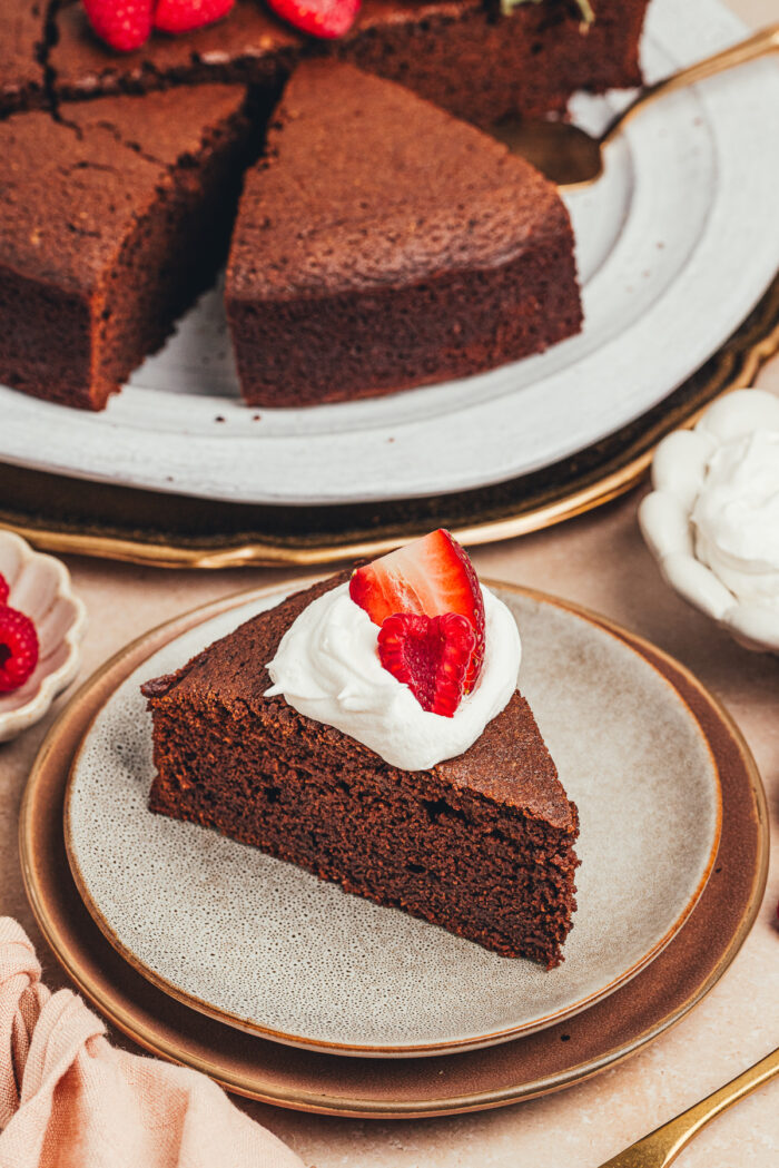 A slice of chocolate ricotta cake with whipped cream and berries on a plate.