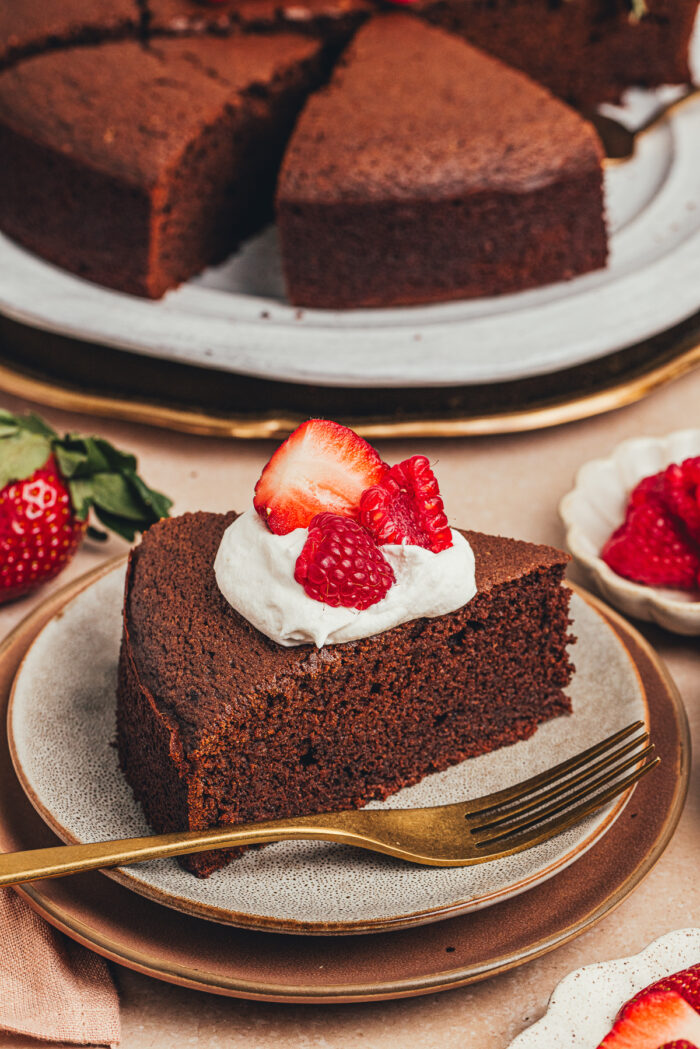 A slice of chocolate ricotta cake with whipped cream and berries on a plate.