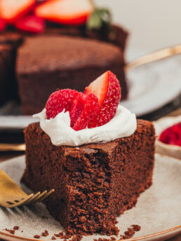 A slice of chocolate ricotta cake with whipped cream and berries with a bite taken out of it on a plate.
