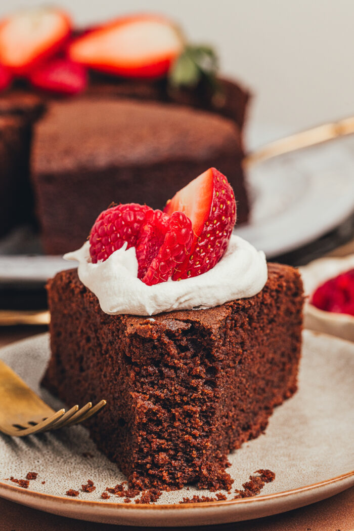 A slice of chocolate ricotta cake with whipped cream and berries with a bite taken out of it on a plate.