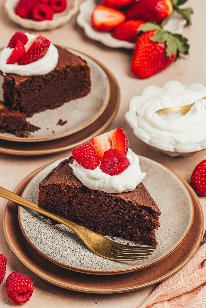 A slice of chocolate ricotta cake with whipped cream and berries on a plate.