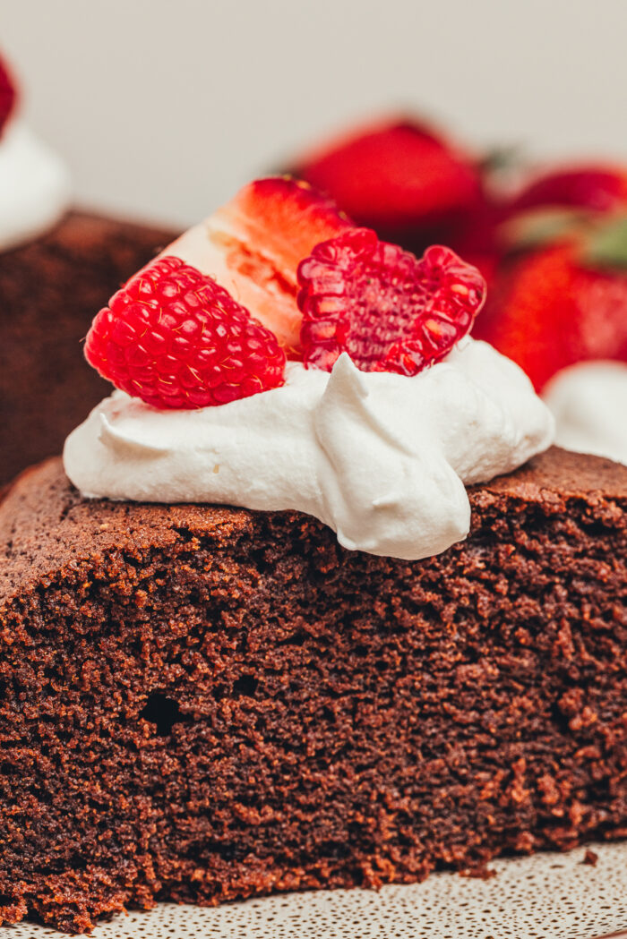 A slice of easy chocolate cake on a plate with a dollop of whipped cream and berries.