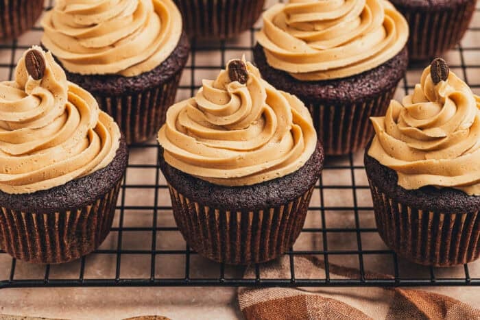 Many chocolate cupcakes with espresso frosting on a cooling rack.