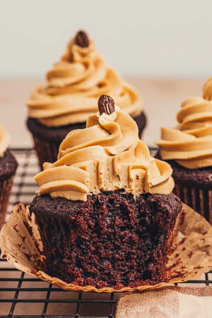 Chocolate espresso cupcakes on a cooling rack with one cupcake with a bite taken out of it.