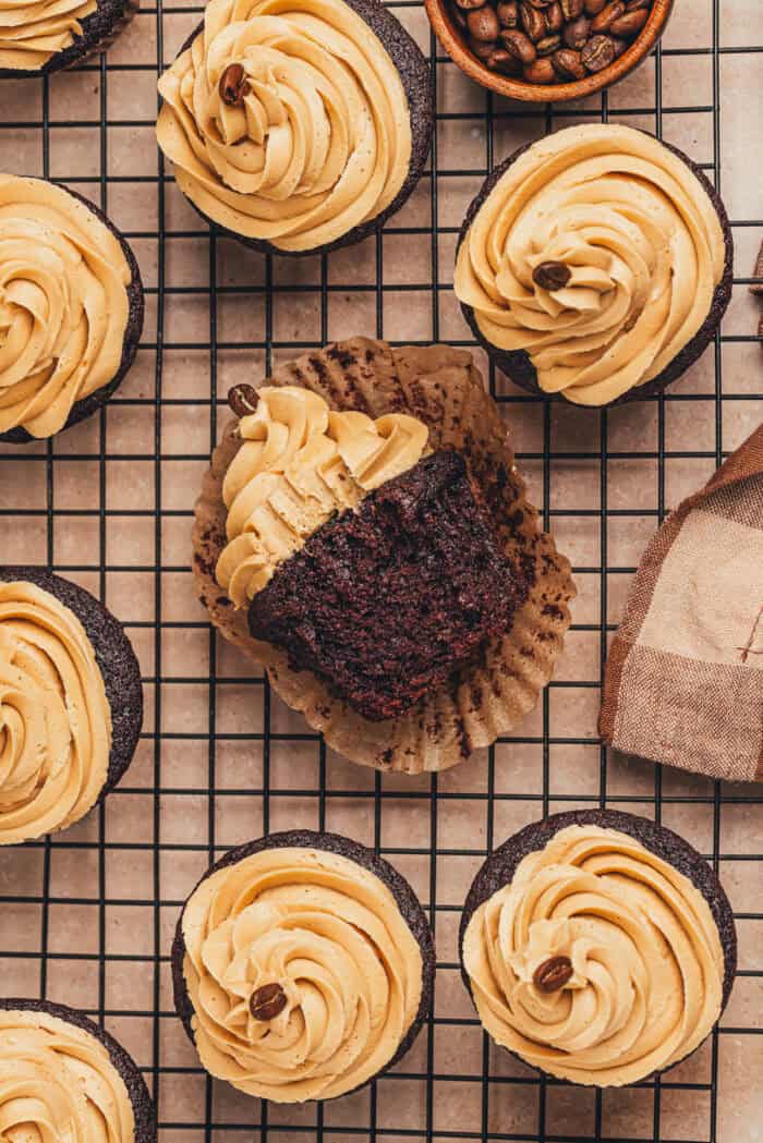 Chocolate espresso cupcakes on a cooling rack with one cupcake on it's side with a bite taken out of it.
