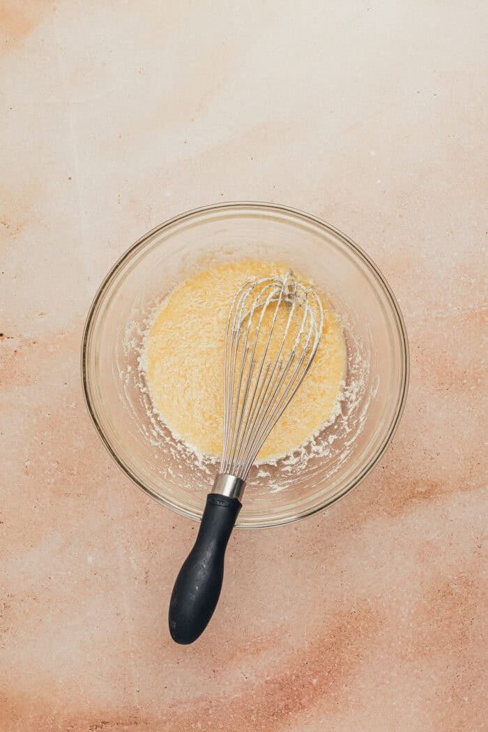 Sour cream, oil, and an egg mixed together in a glass bowl with a whisk.