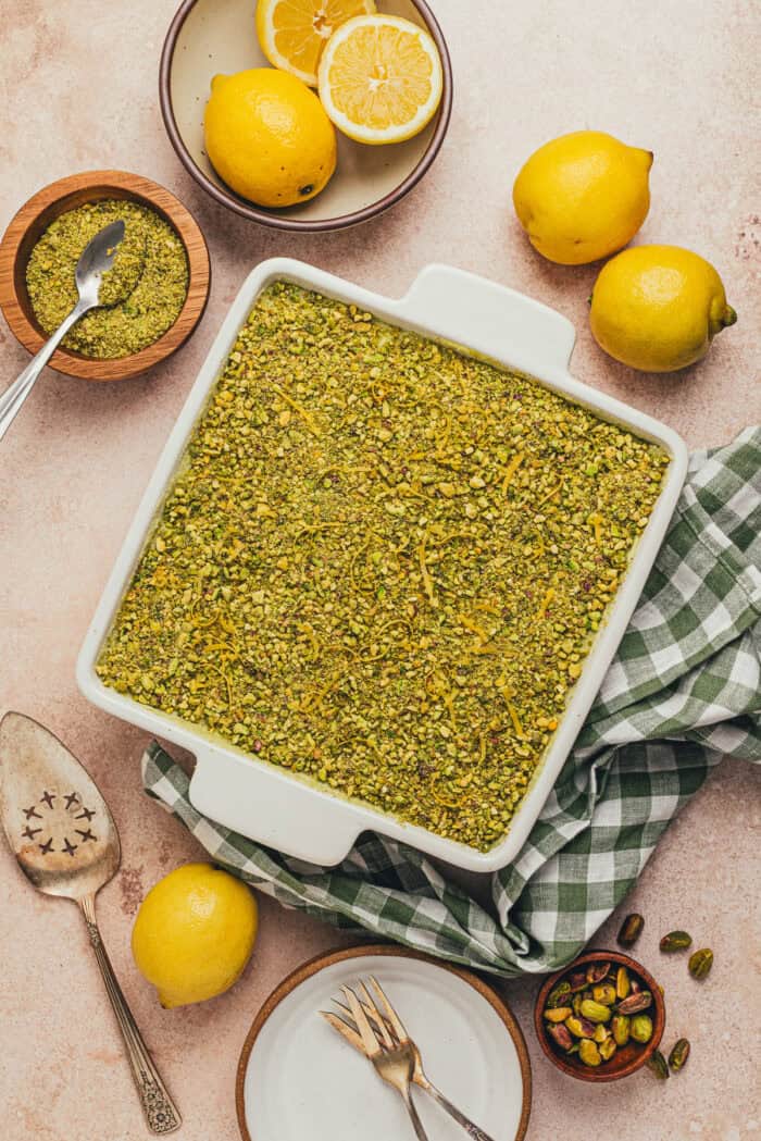 A square pan with pistachio tiramisu and lemons and a green checkered towel.