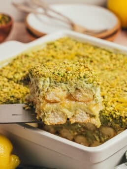 A slice of pistachio tiramisu cake being lifted out of the cake pan.